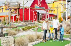 Family exploring a colorful farm-themed miniature golf attractions with a barn.
