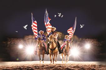 Patriotic horseback performers carrying American flags during a dramatic live stage show.