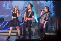 Live music performance on stage with three singers and a guitarist entertaining a packed audience in a Branson theater.