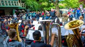 Student musicians performing outdoors in a coordinated band presentation before a large audience, showcasing teamwork and talent