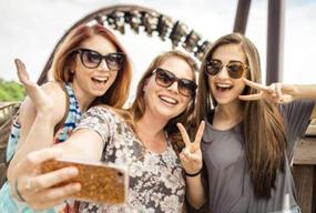 Group of smiling students taking a selfie at a Branson attraction with a roller coaster in the background, capturing memories of a fun, well-supervised trip