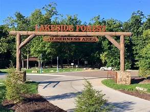 Wooden entrance sign for Lakeside Forest Wilderness Area surrounded by trees and walking paths.