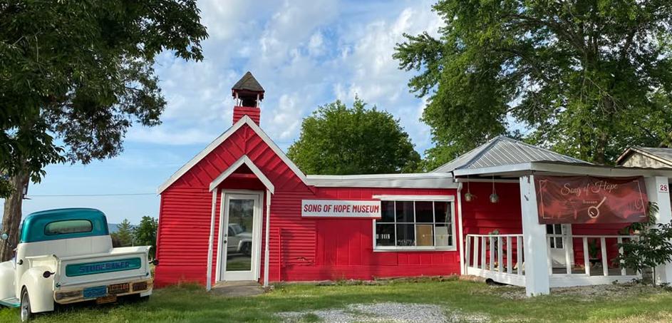 Classic red schoolhouse-style historic building surrounded by trees under a bright sky, offering nostalgic charm.