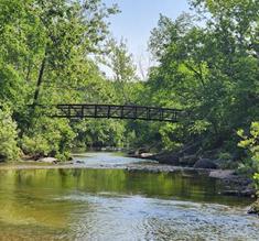 Peaceful Ozarks creek flowing beneath a small wooden bridge surrounded by trees and greenery.