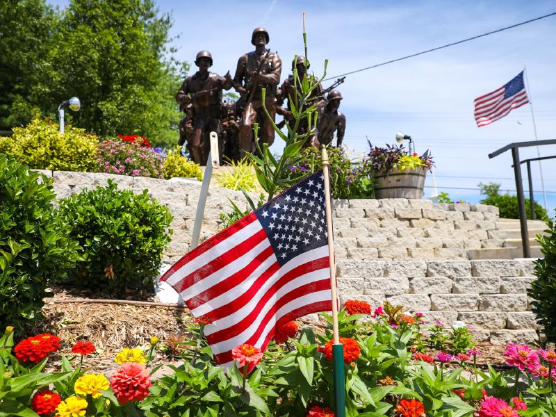 American flag displayed among colorful flowers at a historic memorial with statues and stonework