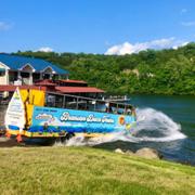 Branson Duck Tours amphibious vehicle splashing into Table Rock Lake, carrying passengers past scenic Ozark hills and waterfront buildings.